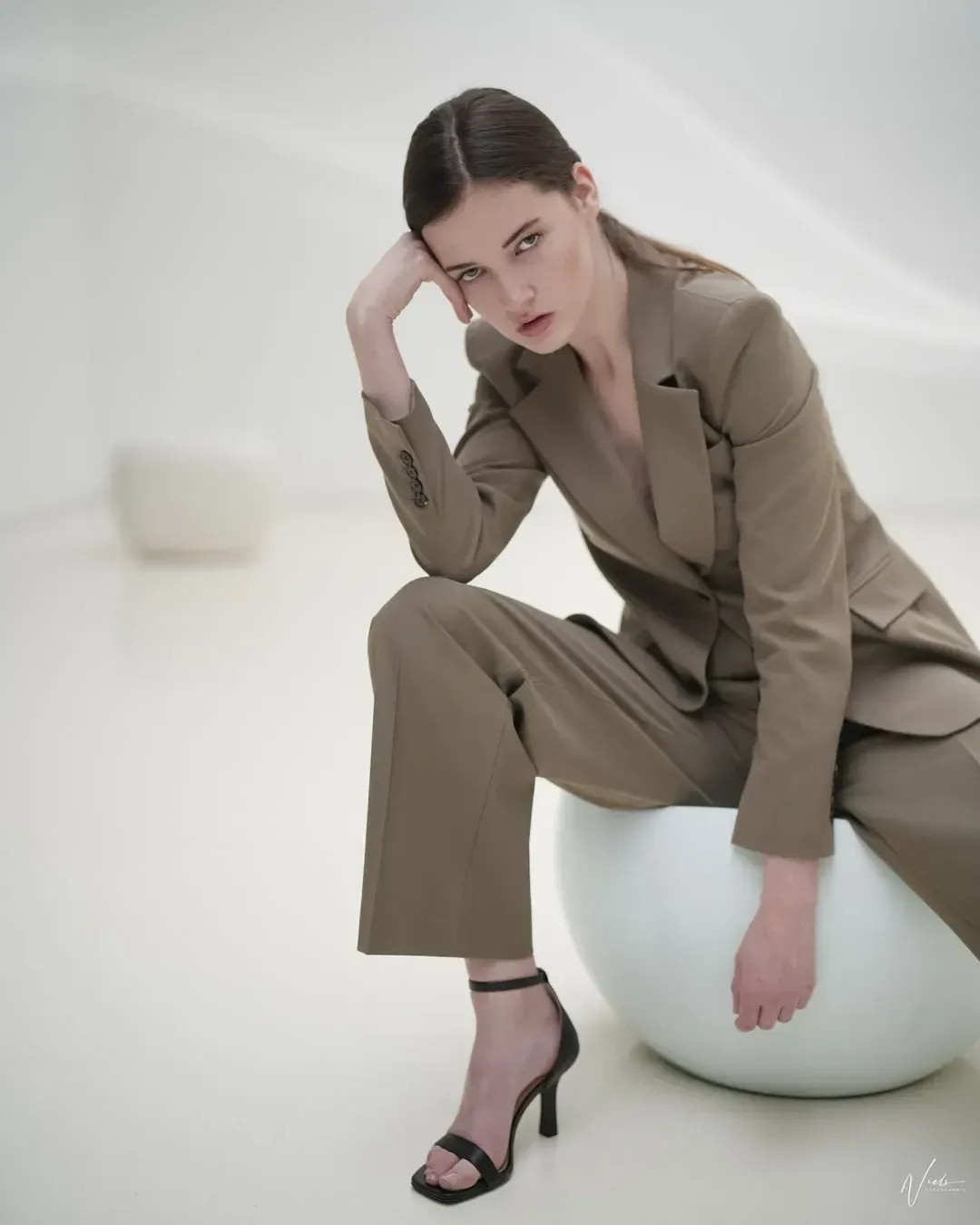 Model im olivgrünen Hosenanzug sitzt auf einer weißen Kugel